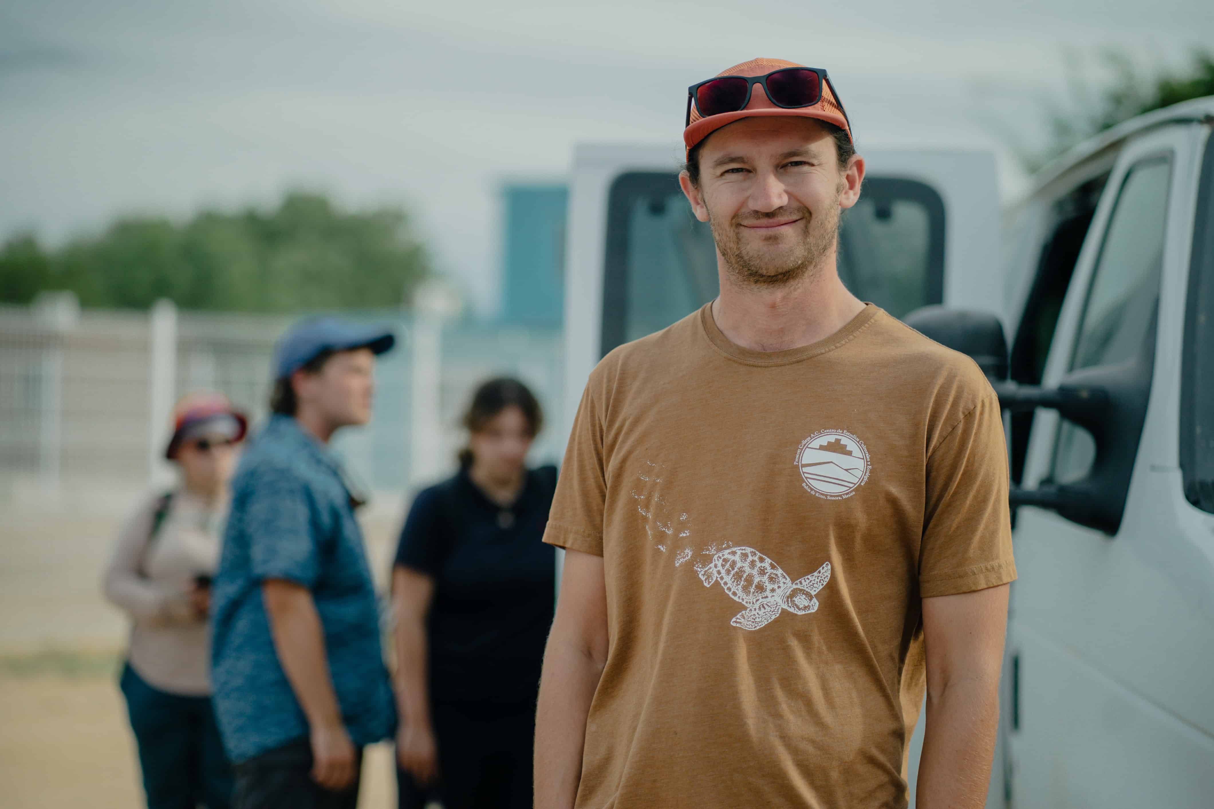 Una persona con la camiseta del Prescott College, sonriendo frente a una camioneta