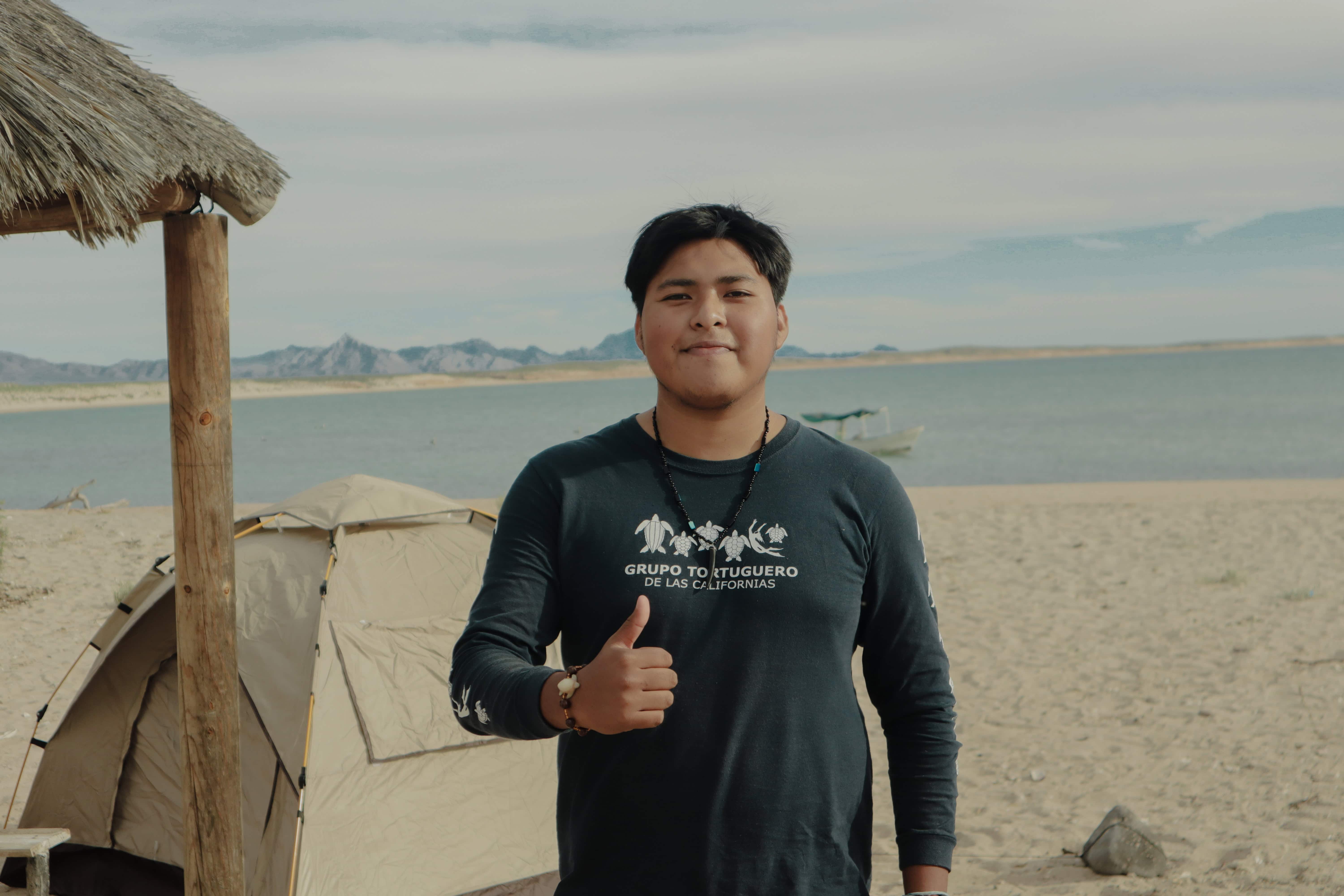 Un joven con la camiseta del Grupo Tortuguero de las Californias hace un gesto de aprobación en la playa